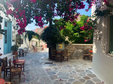 Stone-paved village square with café tables and chairs under pink bougainvillea