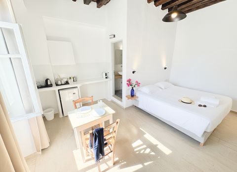 Sunlit studio with large bed, small dining table and kitchenette with fridge