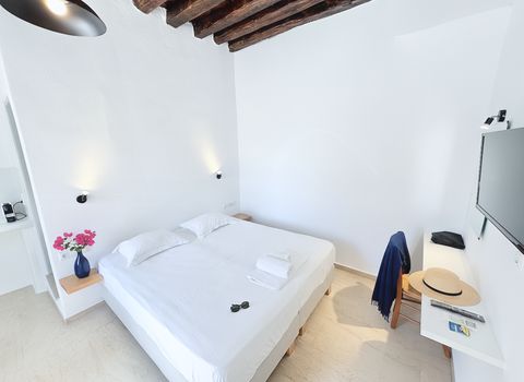 Large bed with white linen under timber ceiling beams, beside a wall-mounted TV