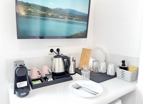 Coffee station with capsule machine, kettle and mugs below a wall-mounted TV